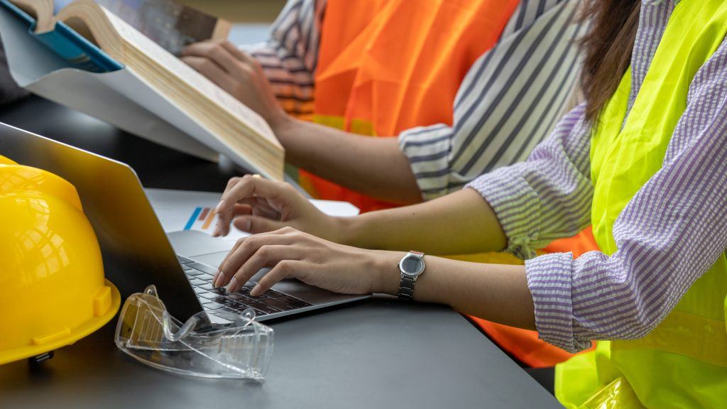 Worker's hands use a computer, performing a search while wearing a construction vest.