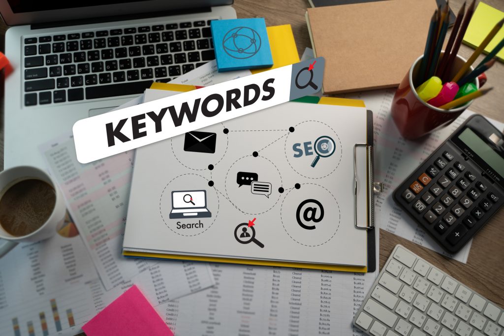 Desktop with scattered marketing notes and a clipboard, the term "keywords" floats digitally over the top inside a search bar.