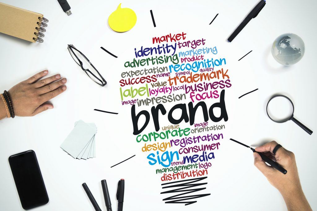 Workers develop branding elements at a desk. Hands are seen over words that form a lightbulb.