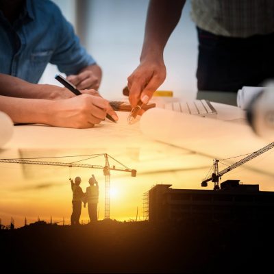 Engineer employees plot out a construction plan, the image blends into the plan in action in front of a setting sun.