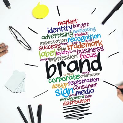 Workers develop branding elements at a desk. Hands are seen over words that form a lightbulb.